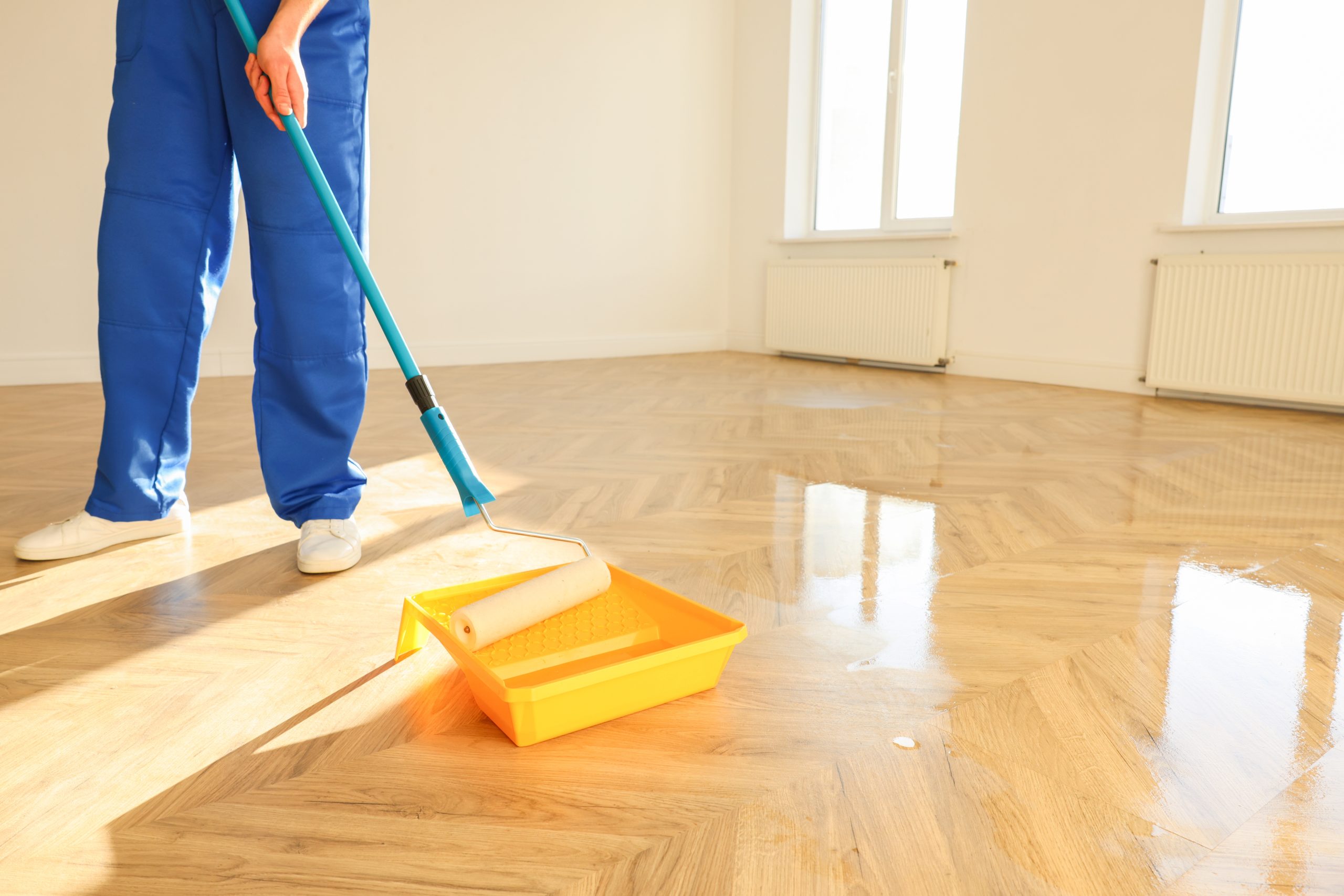 Technician applies clear lacquer with a long-handled roller to a newly sanded chevron parquet floor in a Greenwich home.