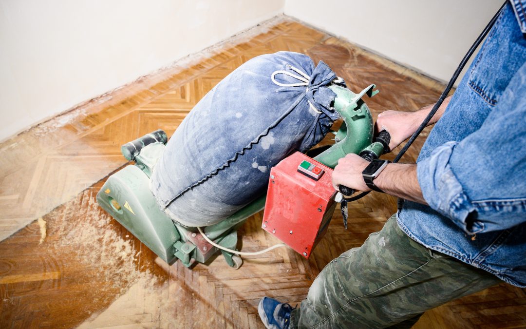Professional wood floor sanding in Greenwich underway on a herringbone parquet floor, showing a technician guiding an industrial drum sander across half-stripped boards.