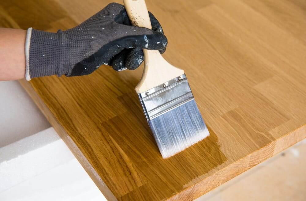 Kitchen Worktop Sanding in Greenwich – close-up of a brush applying oil to a freshly sanded oak butcher-block worktop; oak hardwood kitchen floor.