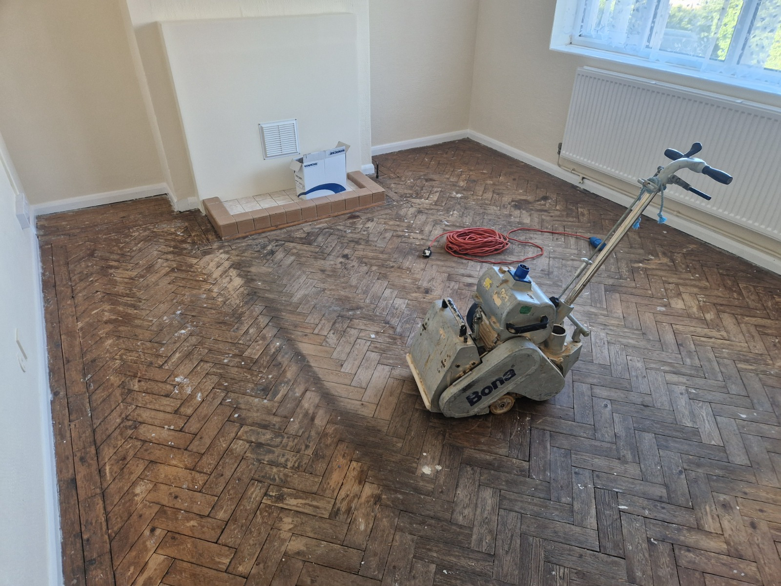Wood Floor Sanding in Greenwich on an oak herringbone parquet floor, with a Bona sanding machine preparing a dusty living room for restoration.