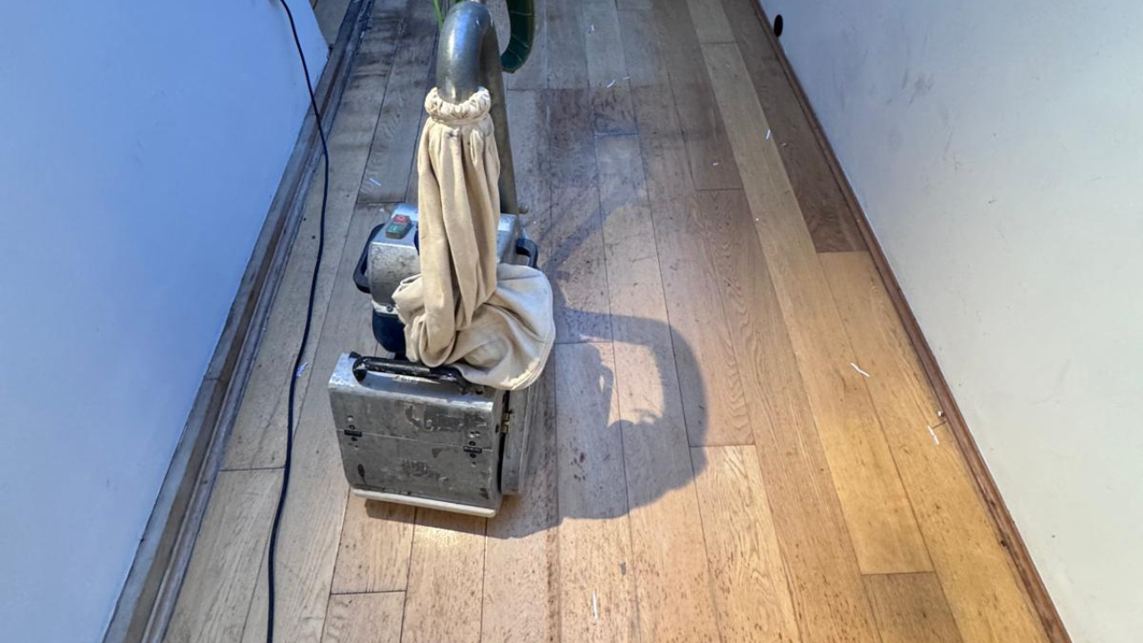 Wood Floor Sanding in Greenwich on an oak plank hardwood hallway floor, with a sanding machine working over worn boards.