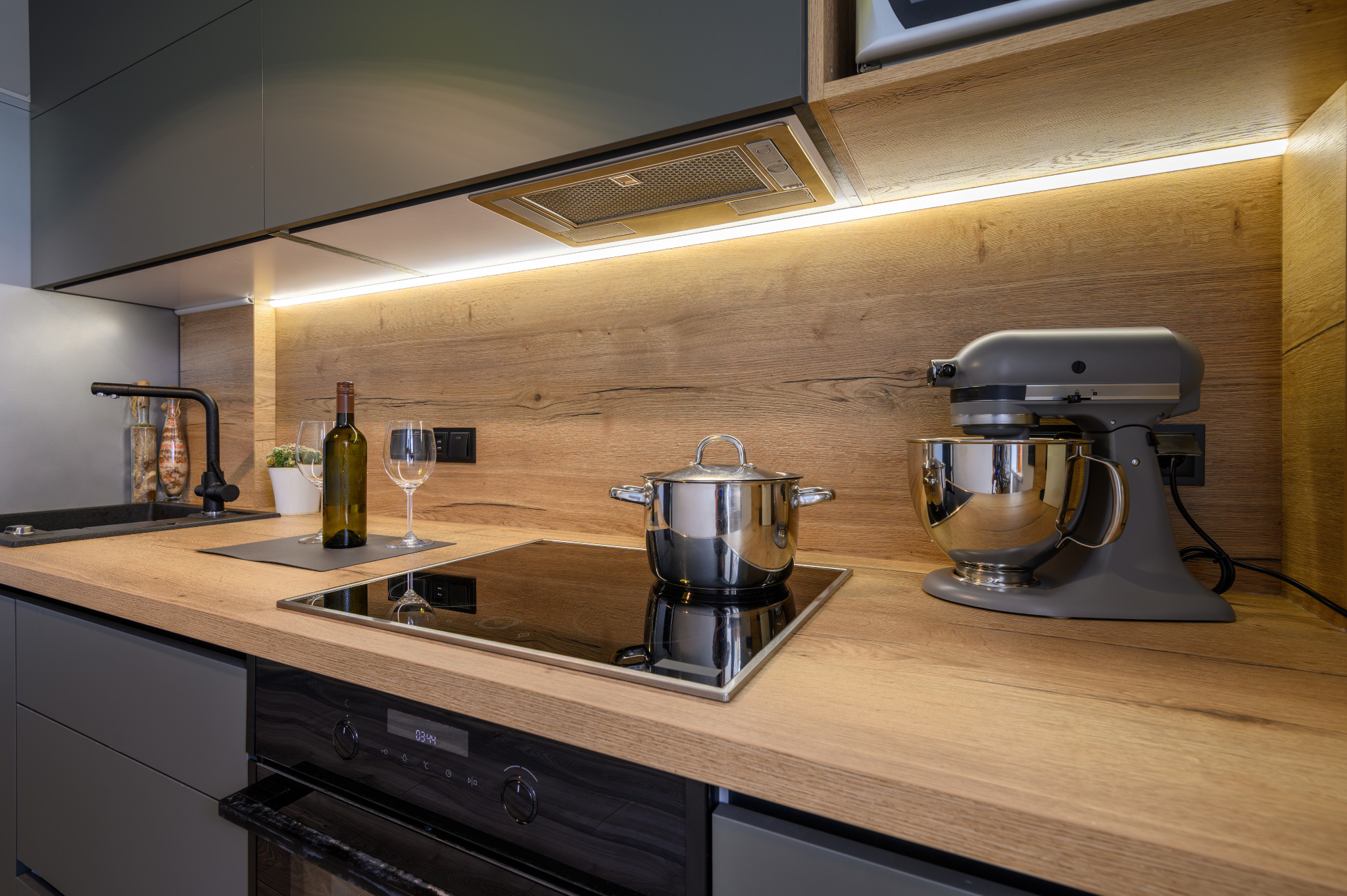 Modern kitchen after Worktop Refinishing in Greenwich, featuring a smooth oak worktop and matching oak engineered wood floor around an induction hob and appliances.