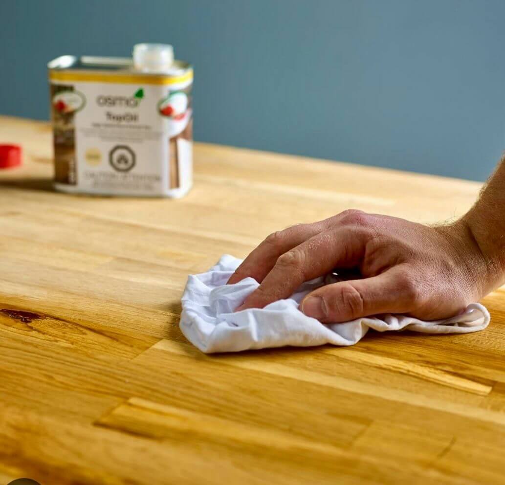 Worktop Refinishing in Greenwich on a solid oak block kitchen worktop with matching oak plank wood floor, as a technician wipes in fresh oil for a smooth, hygienic finish.