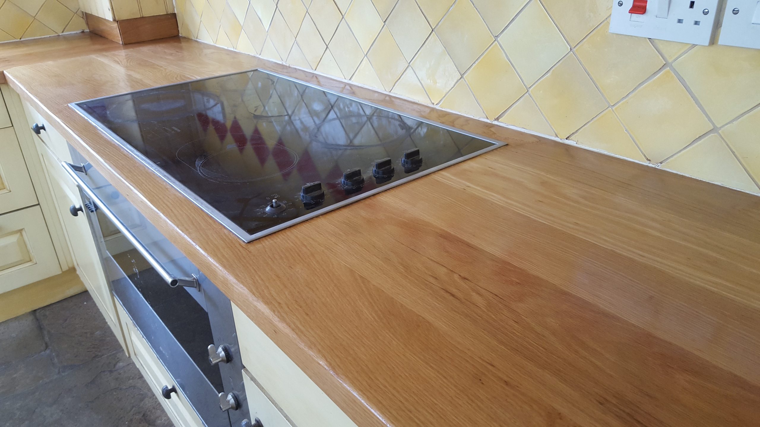 Worktop Refinishing in Greenwich on a solid oak hardwood kitchen worktop, showing a freshly restored smooth surface around a modern electric hob.